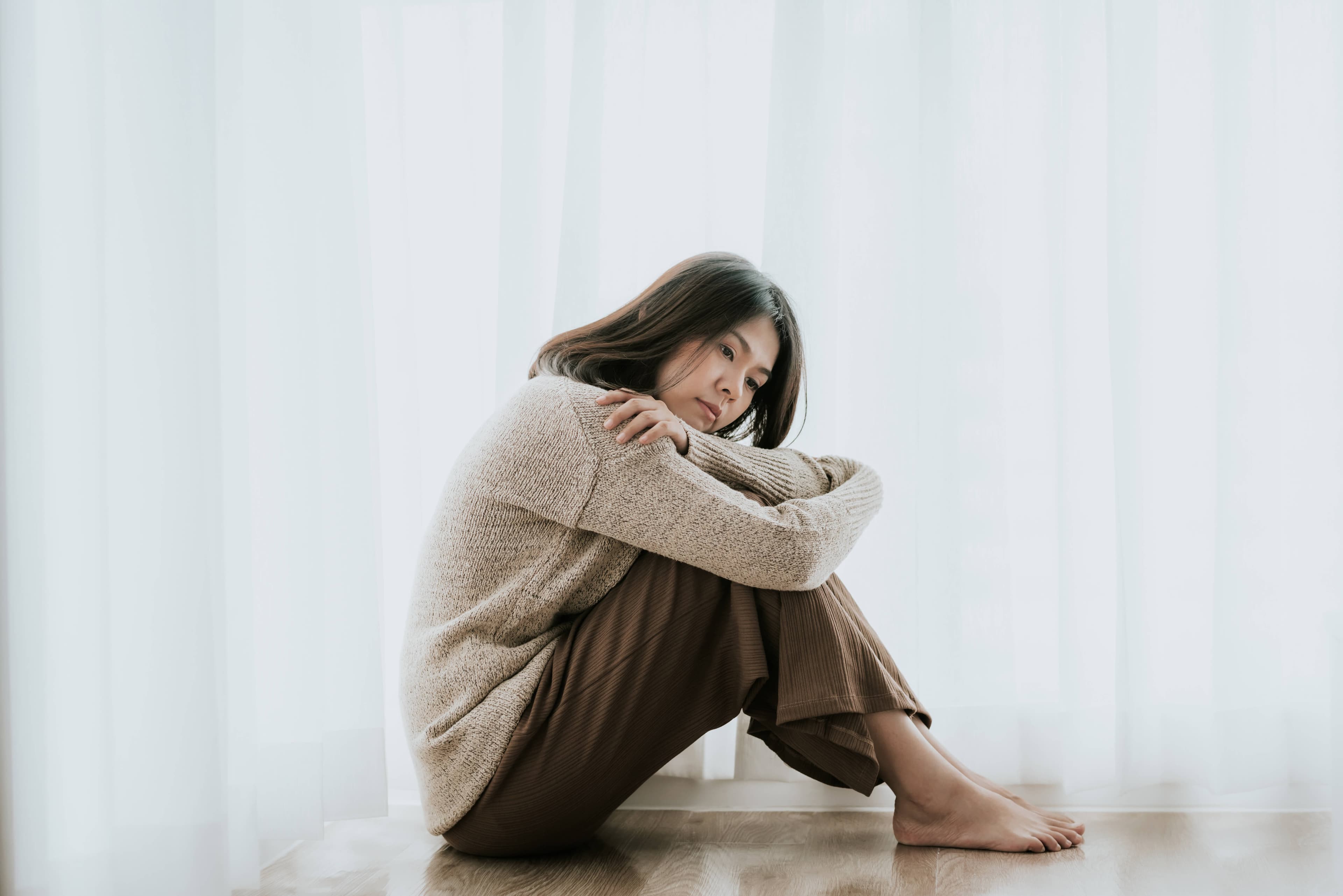 How long does grief last? A person sitting on the floor with hands on their knees, looking sad.