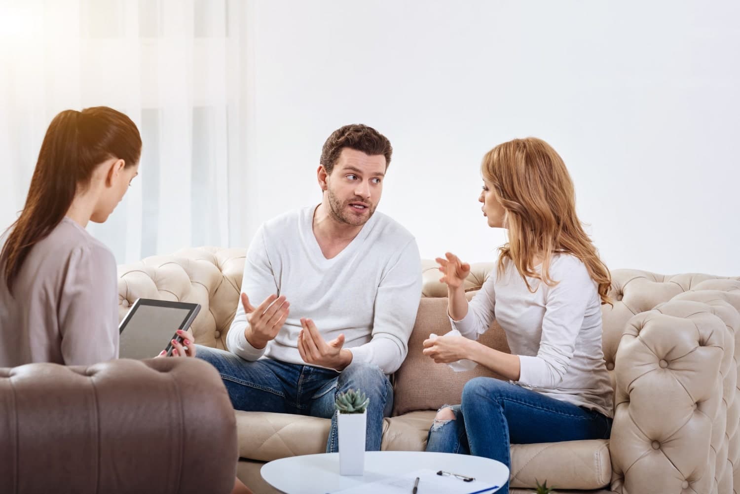 A couple seated opposite a relationship therapist trying to solve an argument through therapeutic tools.