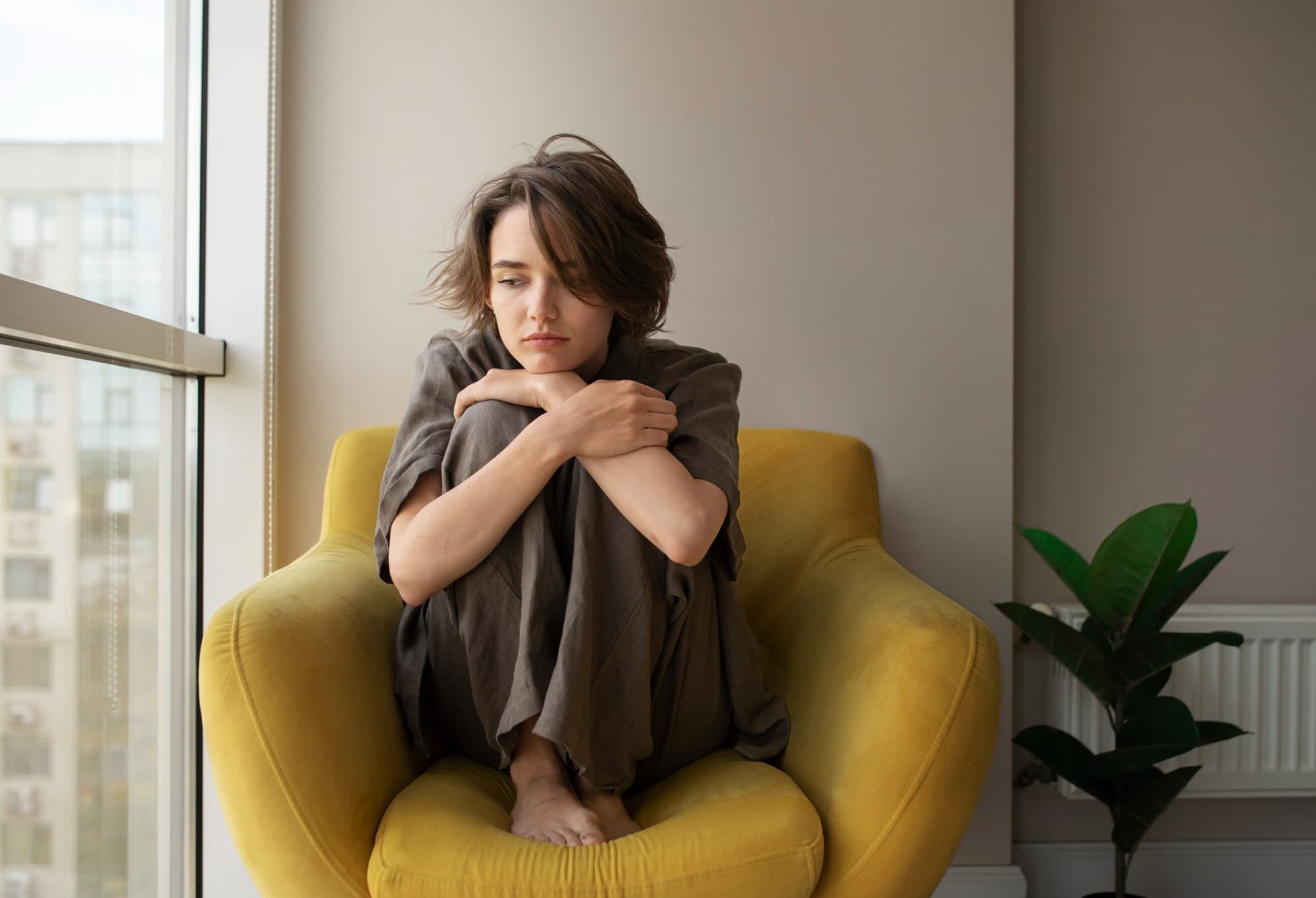 A full shot of a woman with anxiety due to job loss sitting on a chair.