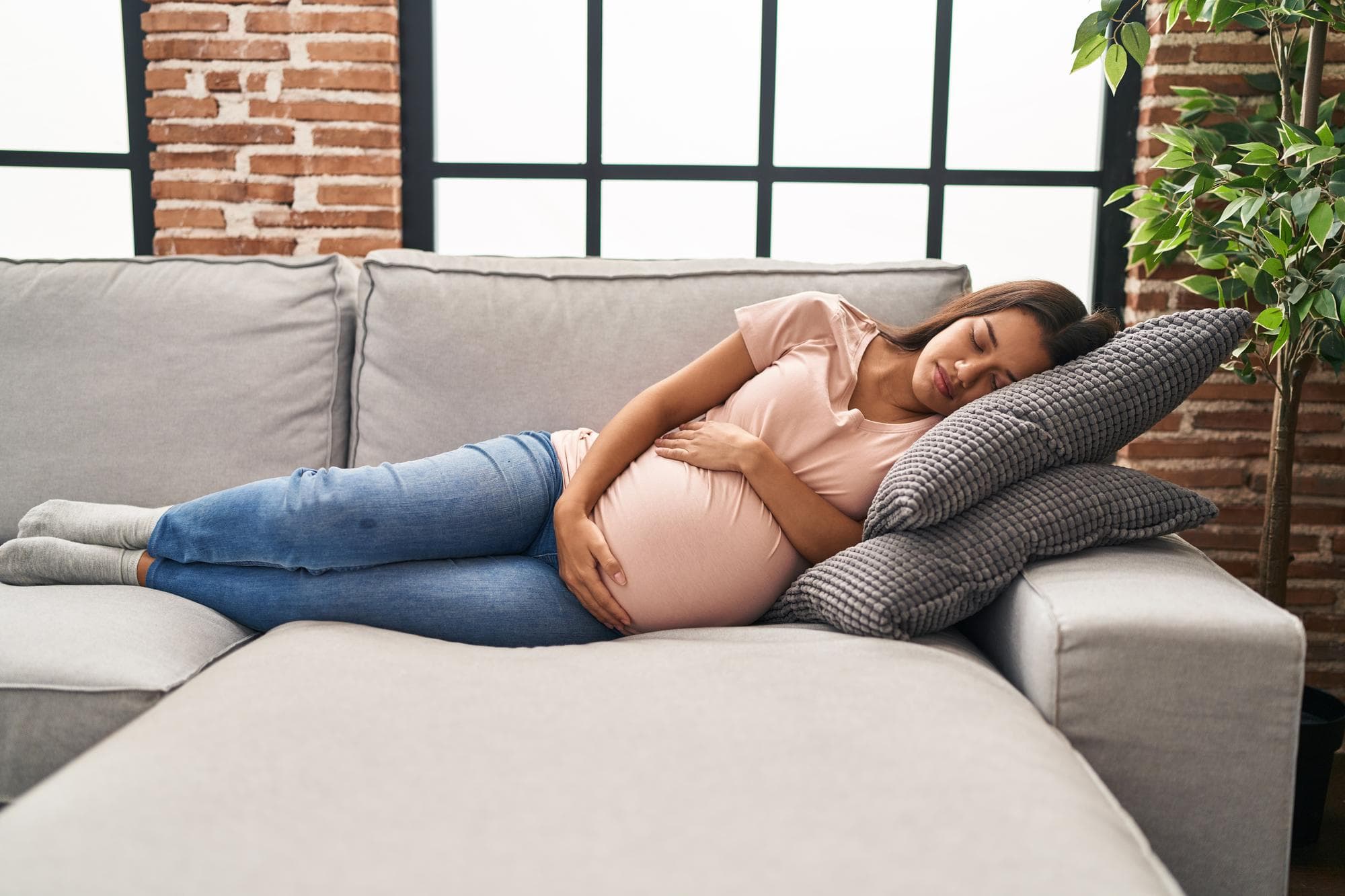 A pregnant mom sleeping on the couch and using relaxation techniques after talking to a therapist in Singapore.