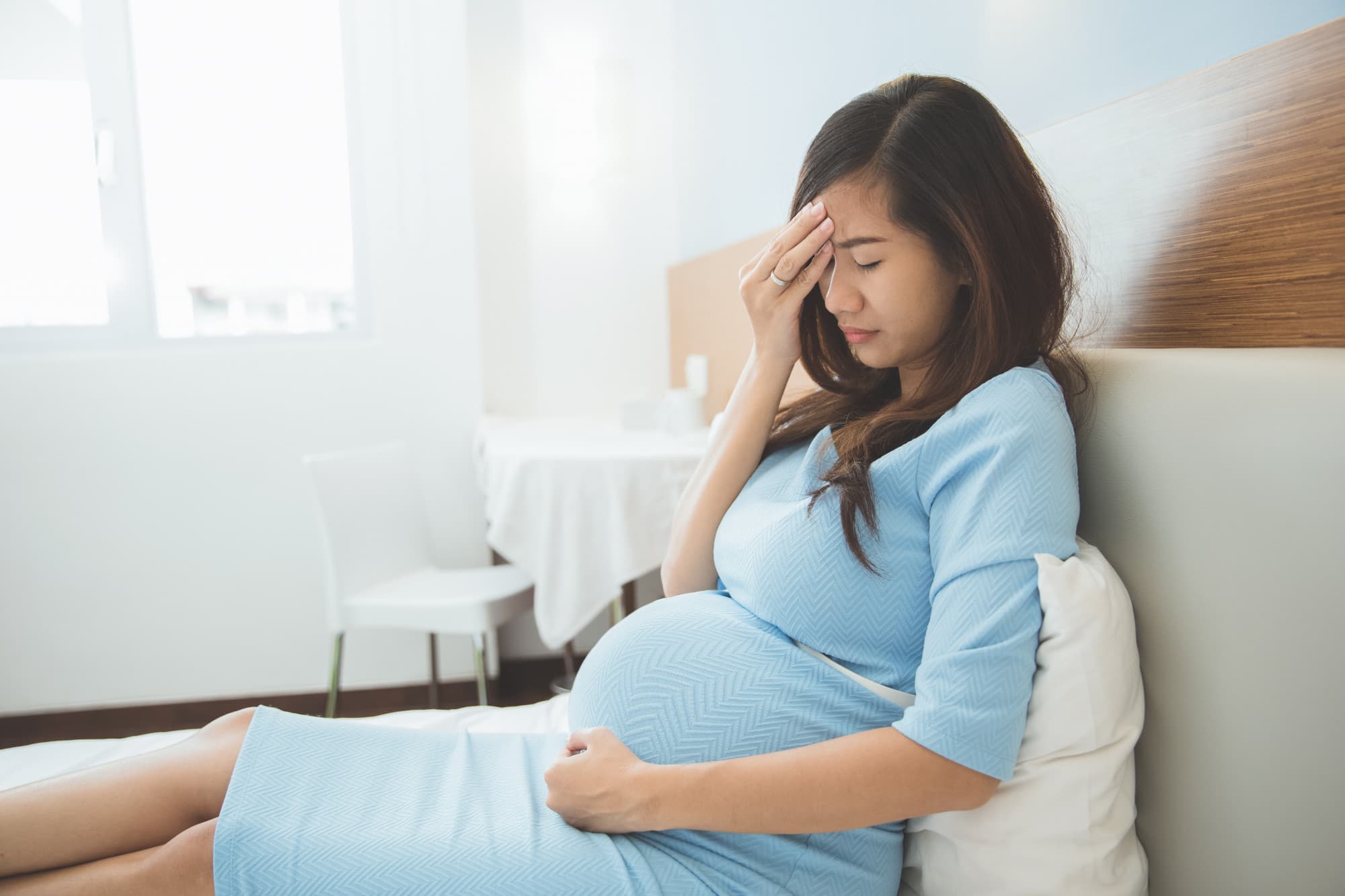 A pregnant mom looking upset due to postpartum symptoms and hoping to talk to a therapist in Singapore.