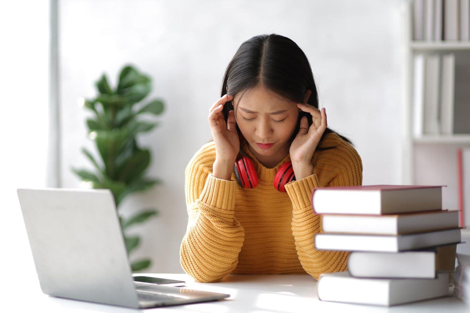 A woman with ADHD symptoms looks stressed while studying. There is a laptop and several books on the table.