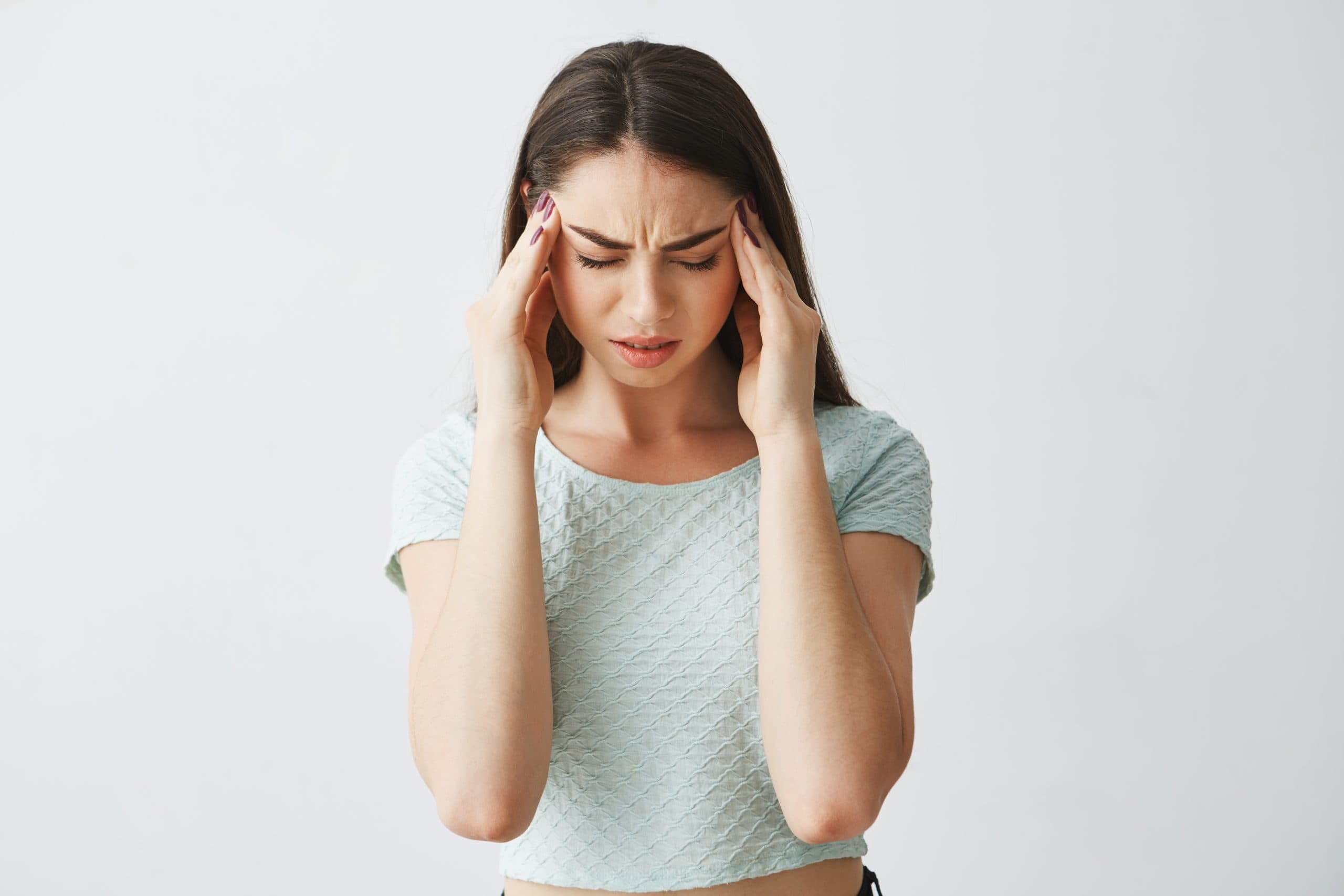 Young beautiful brunette girl frowning touching temples. Headache. Effect of trauma on physical health. Isolated on white background. Copy space.