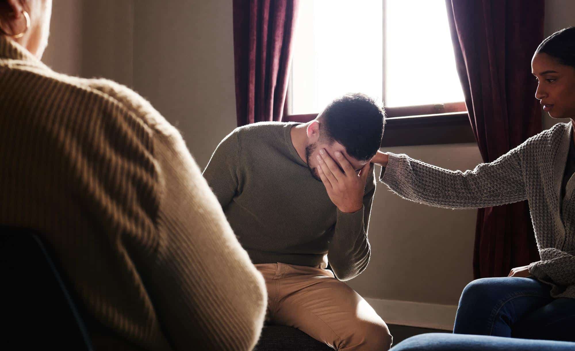A man sitting on a chair and looking upset about the loss of a loved one, considering seeking therapy for grief to cope.