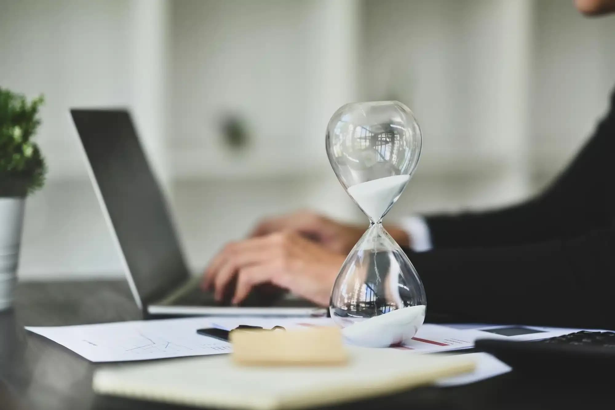 A person engaging in an online counselling session with a hourglass beside the laptop.