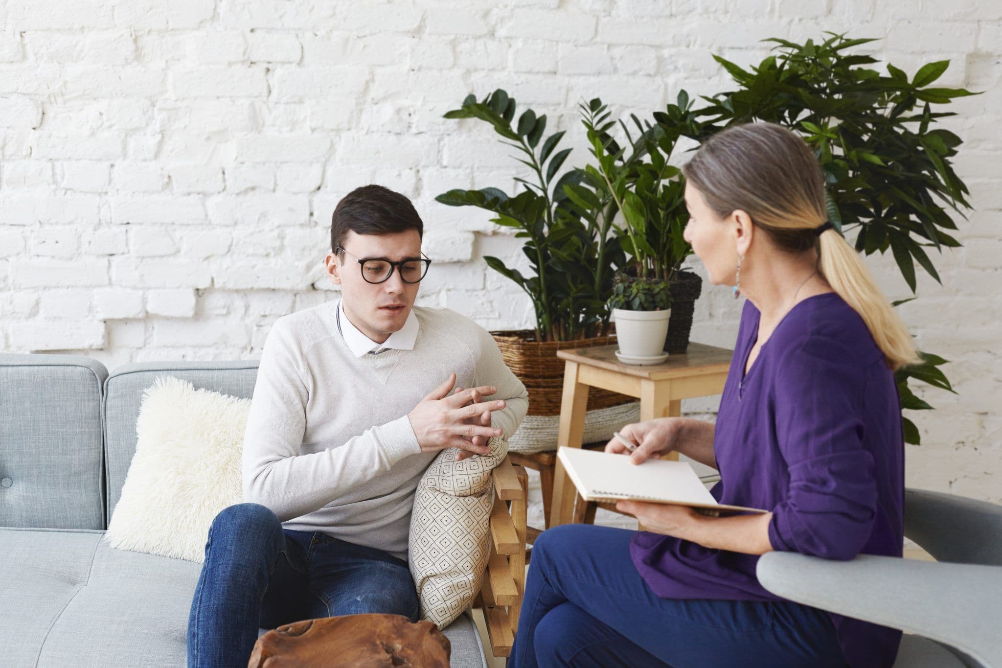 A therapist and a client sit on a couch during counselling in Singapore. The therapist holds a notebook.