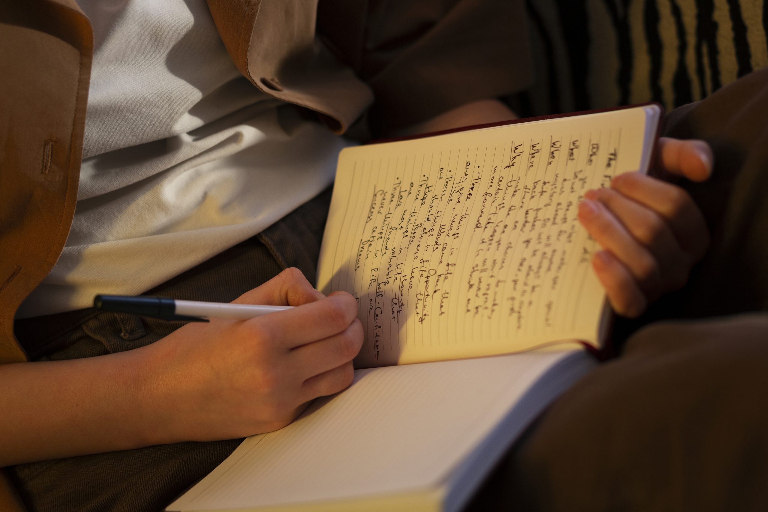 A person sitting and journaling with a pen and notebook. The person is reflecting on their needs for improving relationships.