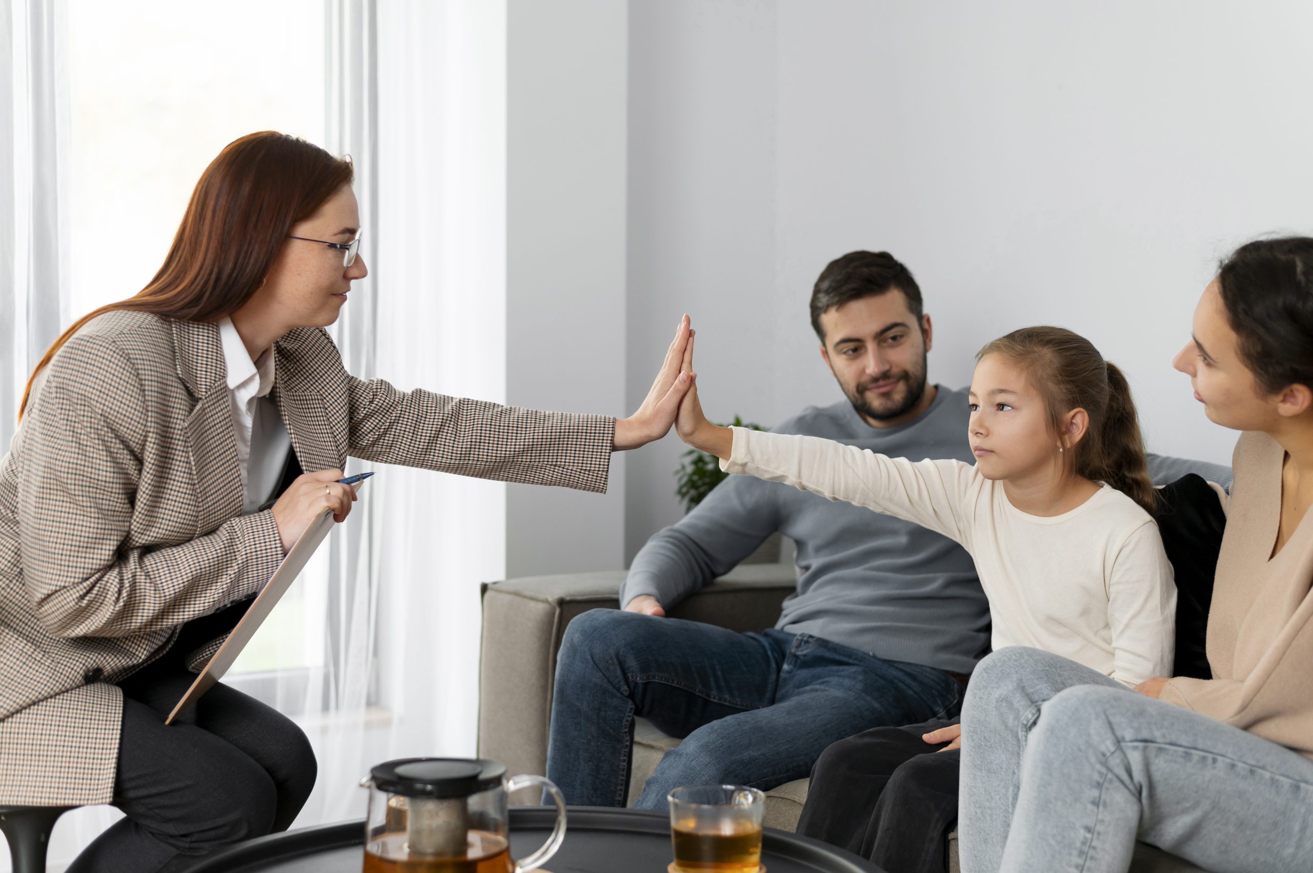 A child gives a high five to a counsellor during counselling services in Singapore. The child is sitting along with their parents opposite to the therapist.