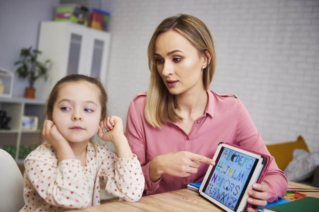 A girl with ADHD looking distracted, and her mother is pointing at the tablet during a study session.