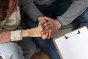 Two people holding hands in mutual support during a counselling session to overcome mental illness.