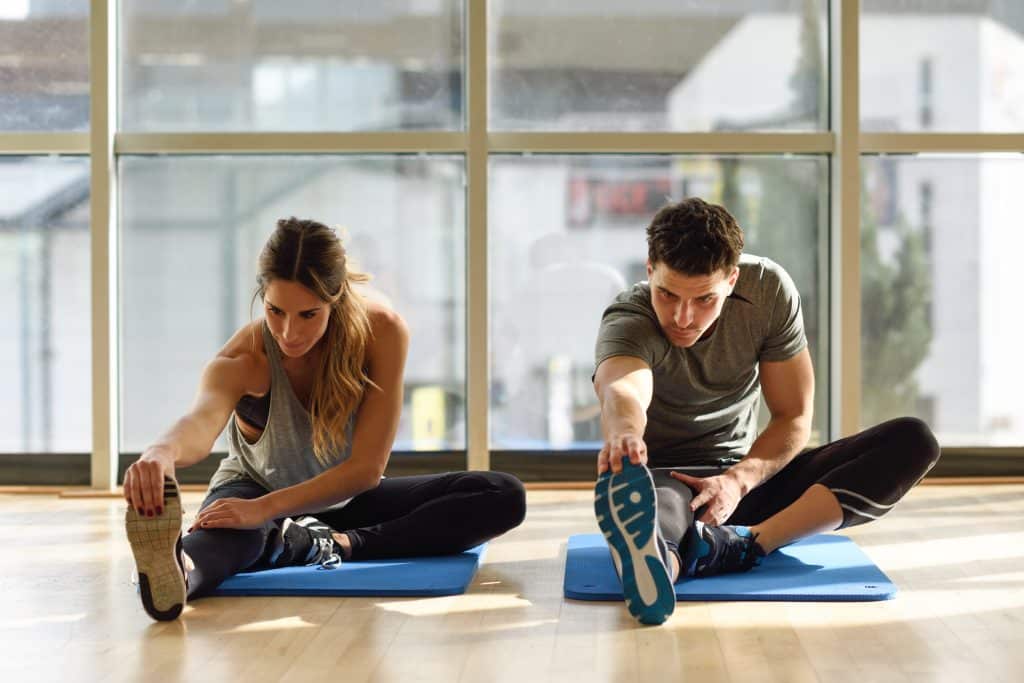 Mental health in Singapore can be maintained thruugh exercise. Two people are stretching on a yoga mat.