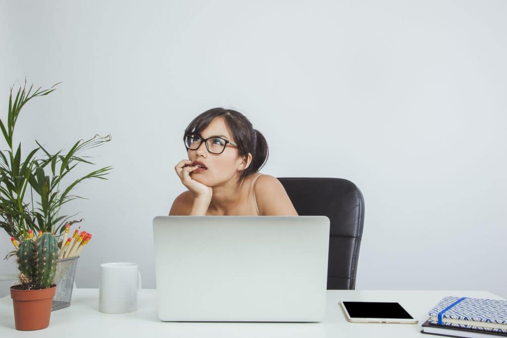 A person sitting and thinking about mental health services in Singapore. The desk has a laptop and a plant pot.