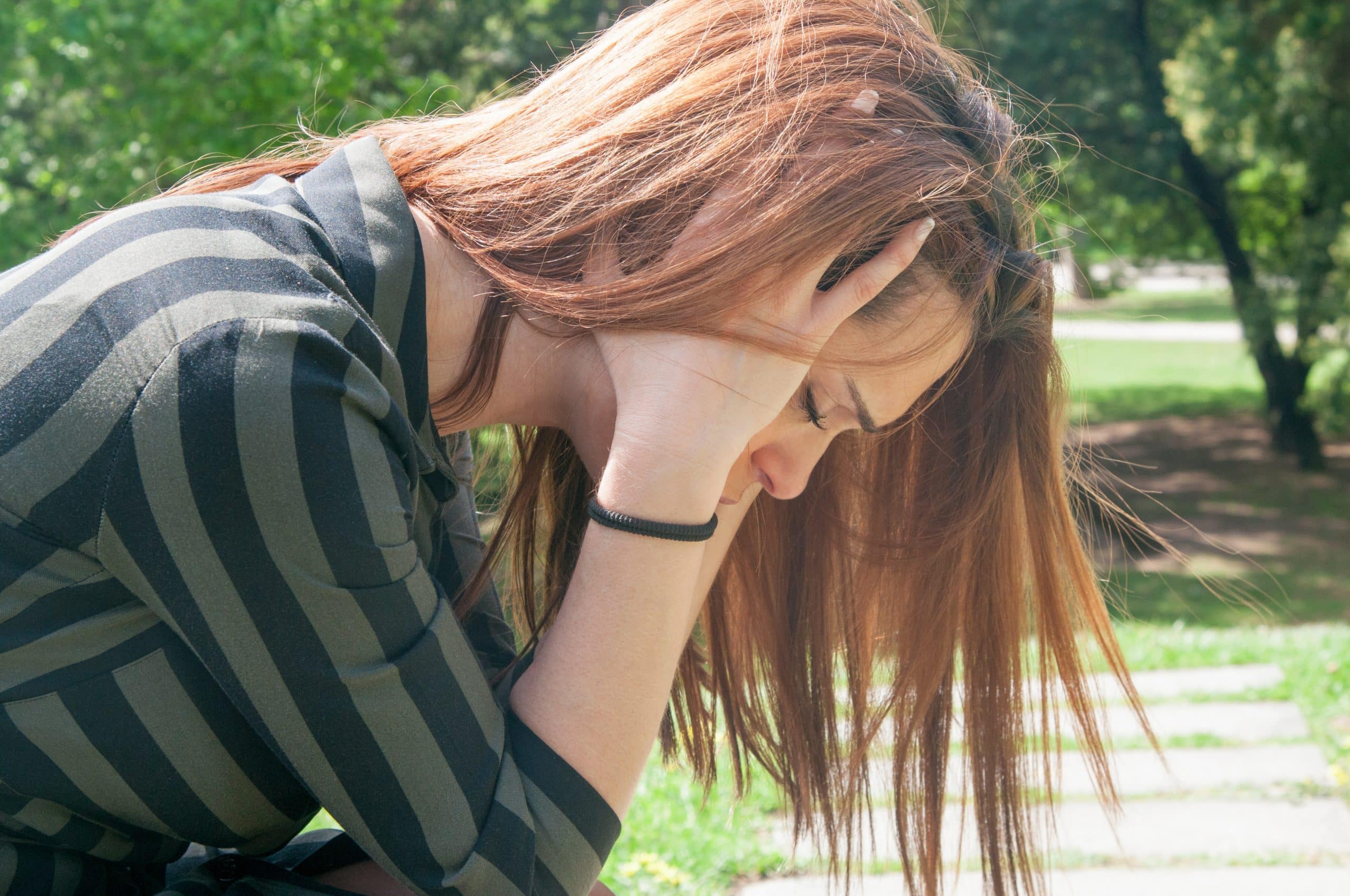 An anxious person holding their head between their hands on a garden due to a psychological disorder.