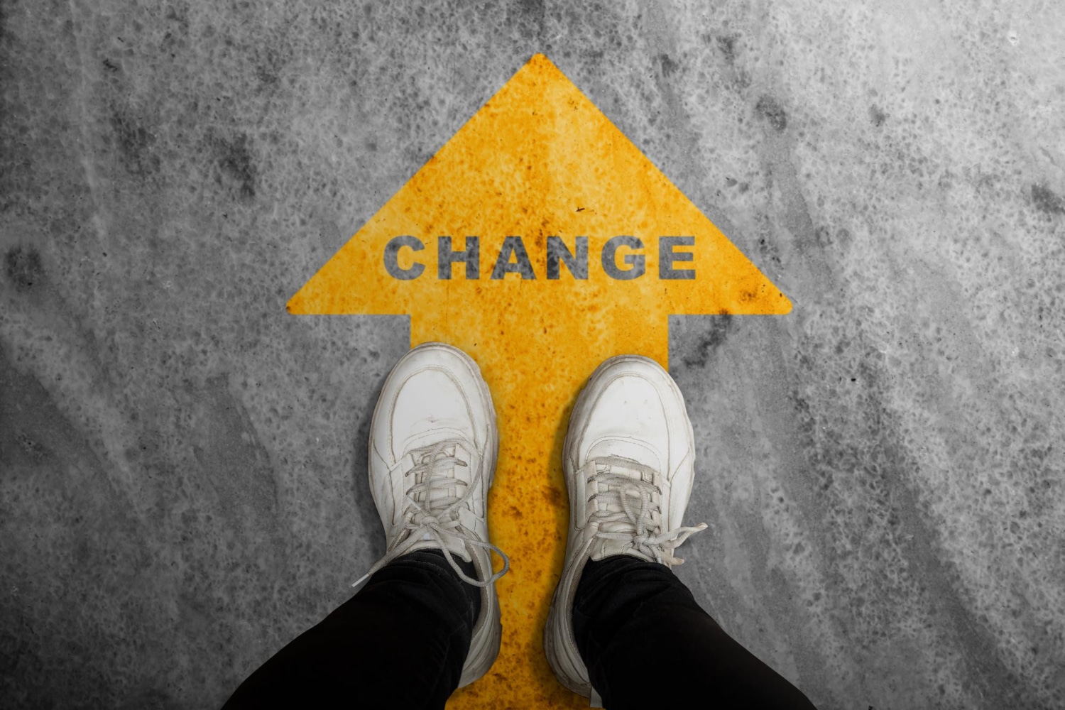 A person in white sneakers stands on a gray concrete floor with a yellow "CHANGE" arrow, ready for a journey of transformation guided by an online therapist.