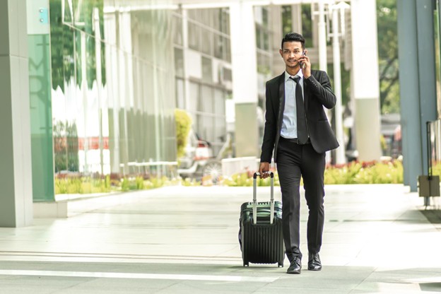 A person in formal clothes, walking to an airport with a trolley, suggesting frequent travel for work.